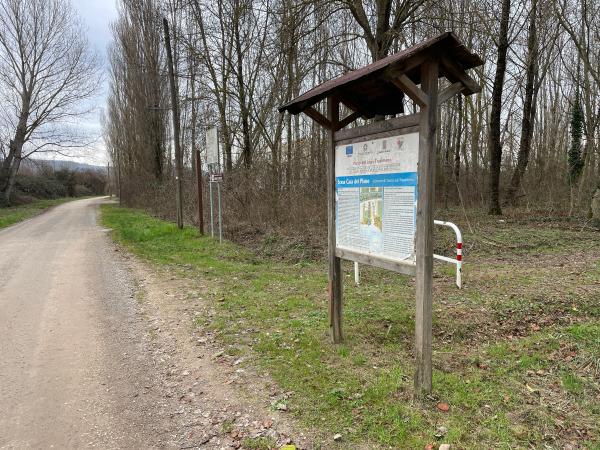 Radweg auf unbefestigtem Weg mit kahlen Bäumen. Rechts ein Informationsschild über den Park und die Oase Casa del Piano.